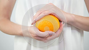 Close-up of an orange in the hands of a girl,fresh and juicy fruit, part of a woman in a white dress on a white background,close-u