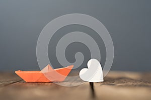 close-up of an orange miniature origami ship with a wooden heart on wooden table