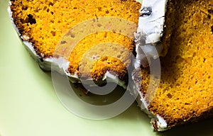 Close up on orange pumpkin pie covered with white icing on green background. Seasonal food