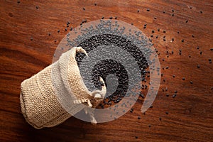 Close-up of  Organic Black Sesame seeds Sesamum indicum or Black Til with shell spilled out from a laying jute bag over a wooden photo