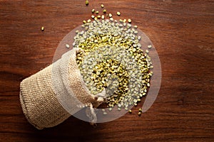 Close-up of Organic green Gram Vigna radiata or spilt green moong dal unpolished spilled out from a laying jute bag over wooden