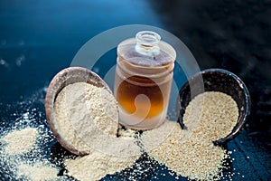 Close up of organic oil of poppy seeds or khus khus in a small glass bottle with raw poppy seeds and powder on wooden surface.
