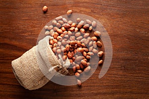 Close-up of organic red-brown peanuts Arachis hypogaea  spilled out from a laying jute bag over wooden brown background