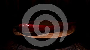 Close up of organic red chili pepper lying on wooden plate isolated on black background. Stock footage. Hot chili pepper