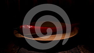 Close up of organic red chili pepper lying on wooden plate isolated on black background. Stock footage. Hot chili pepper