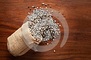 Close-up of Organic split black urad dal Vigna mungo with shell spilled out from a laying jute bag over wooden brown background