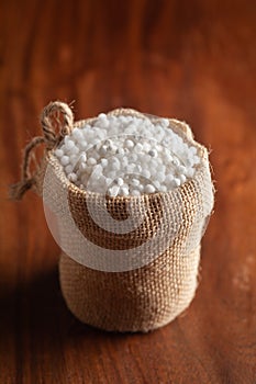 Close-up of organic white sago or sabudana big size in a standing jute bag over wooden brown background