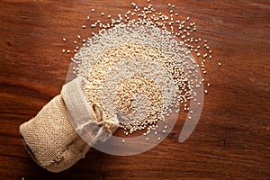 Close-up of Organic White Sesame seedsSesamum indicum or white Til with shell spilled out from a laying jute bag over wooden