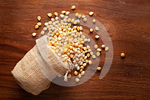 Close-up of organic yellow corn seed or maize Zea mays spilled out from a laying jute bag over wooden brown background photo