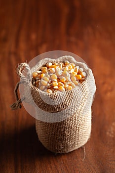 Close-up of organic yellow corn seed or maize Zea mays in a standing jute bag over wooden brown background