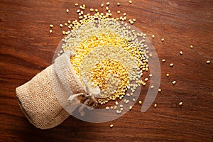 Close-up of Organic yellow Gram Vigna radiata or split yellow moong dal spilled out from a laying jute bag over wooden