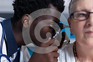 Close up of otology specialist examining ill elderly patient while using otoscope