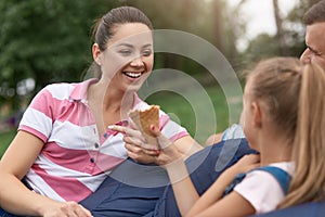 Close up outdoor image of young happy family spending their weekend in park, relaxing while sitting on frameless chair, daughter