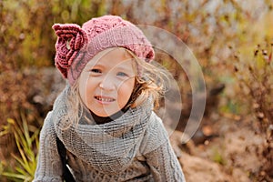 Close up outdoor portrait of adorable smiling child girl in pink knitted hat and grey sweater