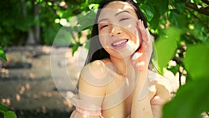 Close up outdoor portrait Beautiful young Chinese Asian woman perfect skin posing outside sunny summer day green foliage