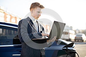 Close up outdoor portrait of concentrated purposeful likable young businessman, typing a message on laptop pc, while