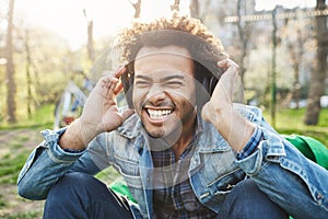 Close-up outdoor portrait of handsome african man with afro haircut holding hands on headphones while listening to music