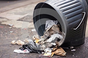 close-up of overflowing trash bin, with garbage spilling out onto the ground