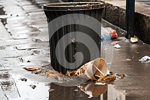 close-up of overflowing trash bin, with garbage spilling out onto the ground