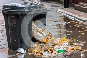 close-up of overflowing trash bin, with garbage spilling out onto the ground