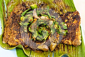Close-up overhead view of grilled stingray fish with spices topped with okra vegetable on banana leaf popular food in