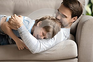 Close up overjoyed father and son hugging, lying on couch