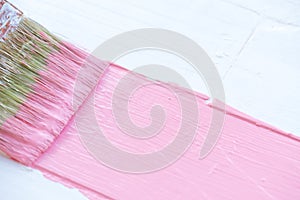 Close up paintbrush painting pink color on a white wooden