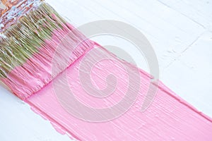 Close up paintbrush painting pink color on a white wooden table