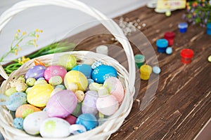 Close up painted Easter eggs in a basket and paintbrush resting on wood plank table