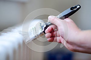 Close up of painter arm painting a heating radiator with paint roller. Professional Workman Hand holding Dirty Paintbrush.