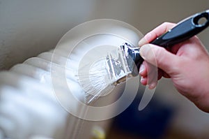 Close up of painter arm painting a heating radiator with paint roller. Professional Workman Hand holding Dirty Paintbrush.