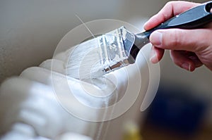 Close up of painter arm painting a heating radiator with paint roller. Professional Workman Hand holding Dirty Paintbrush.