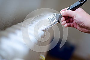 Close up of painter arm painting a heating radiator with paint roller. Professional Workman Hand holding Dirty Paintbrush.