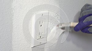 Close up of painter hands with gloves painting the wall around power outlet