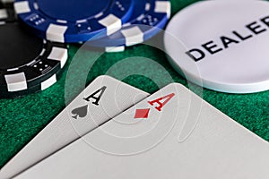 A close-up of a pair of aces, diamonds and spades, on standard playing cards. on a green felt surface with black and blue betting