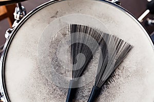 Close-up of a pair of black drum brushes on a white shabby drum. Concept concert, live music, performance, musical evening in a