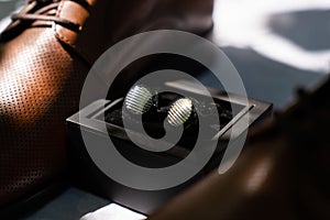 Close-up of a pair of cufflinks and brown groom shoes on a blurred background