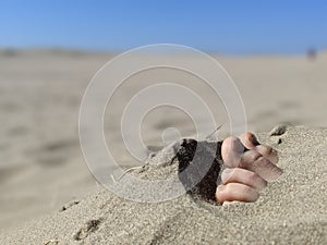 Close up of a pair of feet and toes sticking out of beach sand photo
