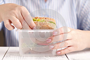 Close up on pair of female hands removing a healthy wholesome wholemeal bread ham sandwich from her lunch box during lunch break