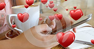 Close up of a pair of female hands texting beside a cup of coffee and a pen and notebook