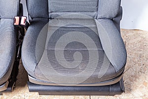 A close-up of a pair of front seats covered in gray fabric with a curly pattern with plastic seat belt locks taken before
