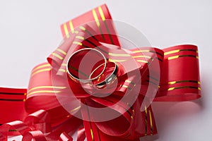 Close-up of pair Gold Wedding rings on red wedding ribbon bow