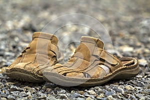 Close-up of pair of old worn comfortable man classic leather soft brown summer shoes sandals on outdoor stone pebbles background.