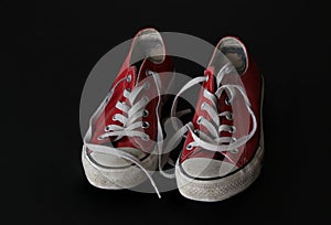 Close up of pair of sneakers - red and white vintage worn out shoes - youth hipster shoes on black background - top view