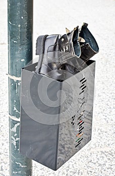 close up of a pair of used black boots made in black leather abandoned in a black bin. Boots and bin at a post in the sidewalk of