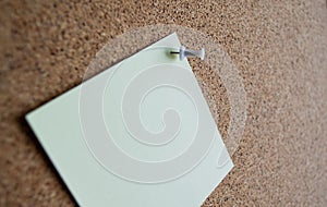 Close up of a pale green paper note on a cork Board, attached with a white pushpin. Copy space