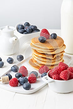 Close up of pancakes in stack with blueberries, raspberries and milk on table and white background, vertical,