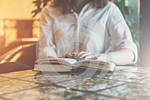 Close-up of paper book, notebook, diary on table in cafe. Businesswoman in white shirt sitting at table and reading book