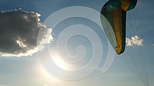 Close-up of a paraglider parachute fluttering in the wind, against a background of blue sky, clouds and sun
