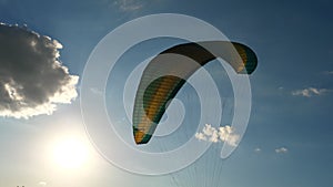 Close-up of a paraglider parachute fluttering in the wind, against a background of blue sky, clouds and sun